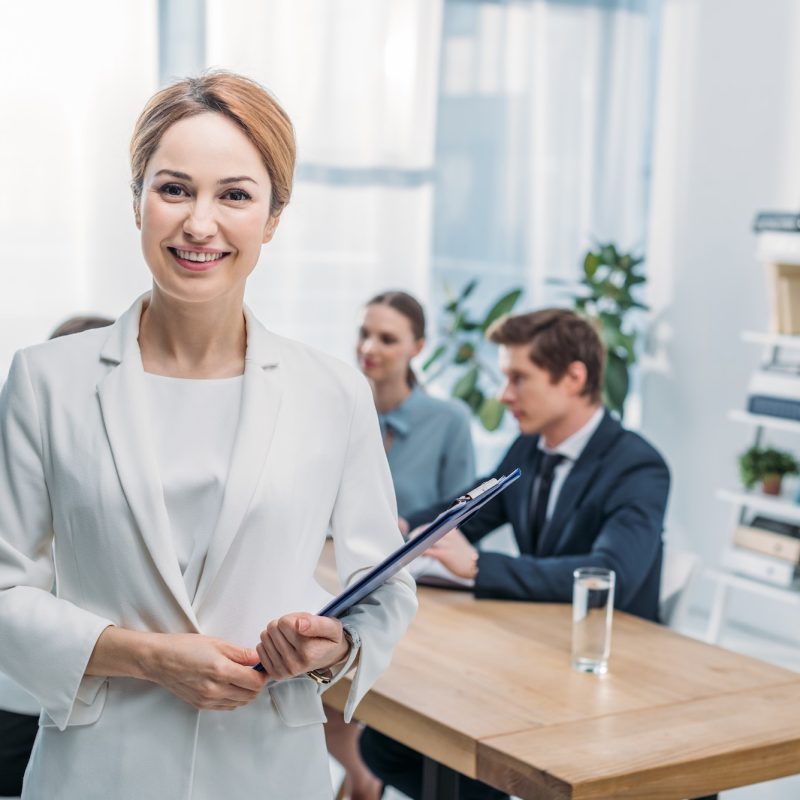 selective-focus-of-cheerful-recruiter-standing-with-clipboard-near-coworkers.jpg